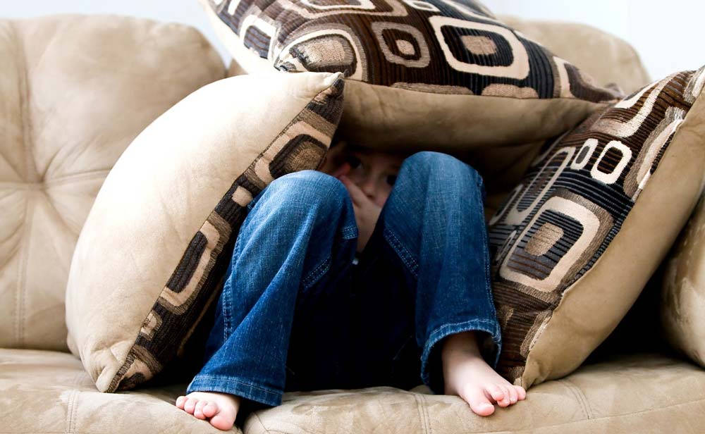 Mensch versteckt sich unter Couchkissen