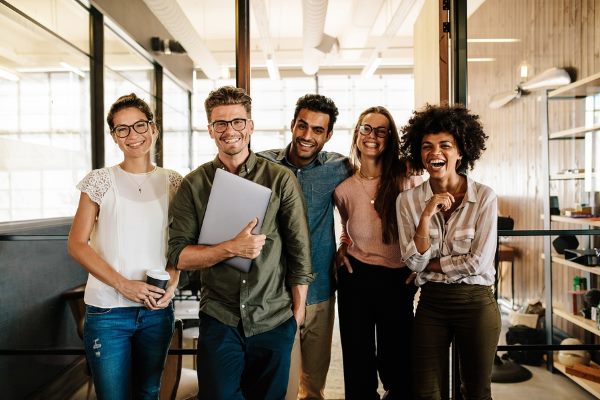 a group of young people smiling while standing in the office